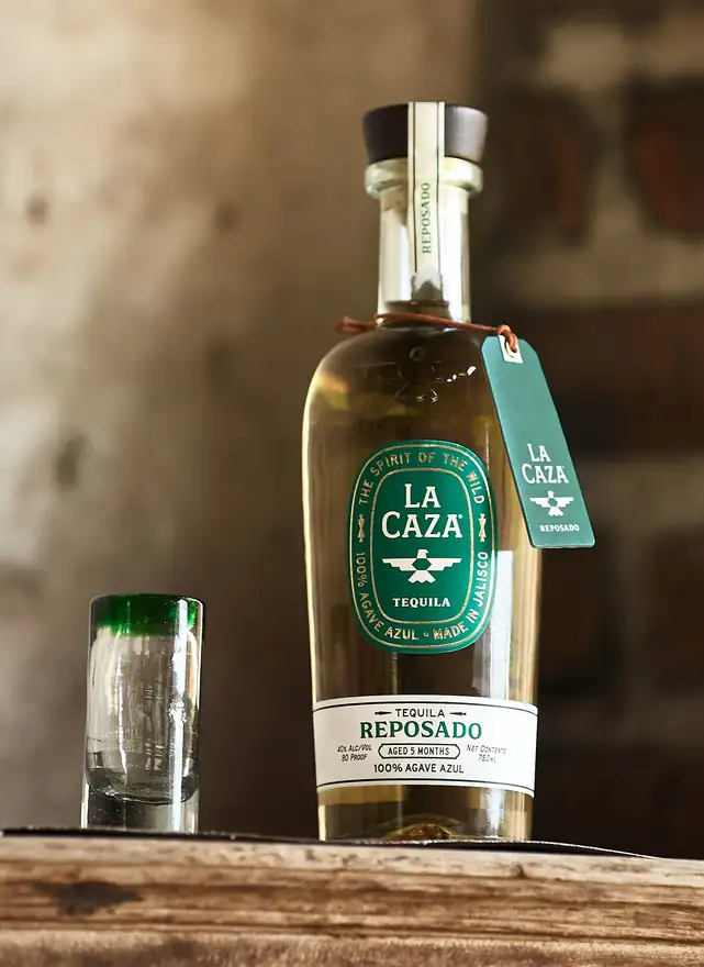 La Caza Reposado beside a green-rimmed hand-blown shot glass on a wooden beam