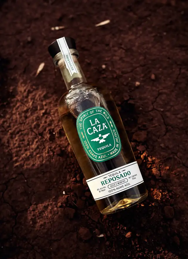 La Caza Reposado with its green oval label, lying in cracked red earth