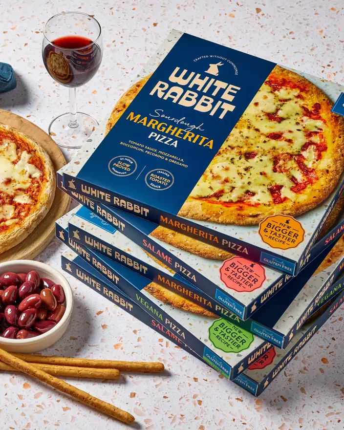 A stack of White Rabbit pizza boxes with a glass of red wine, olives and breadsticks