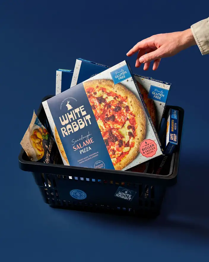 A hand placing a White Rabbit Salame pizza into a shopping basket full of the range