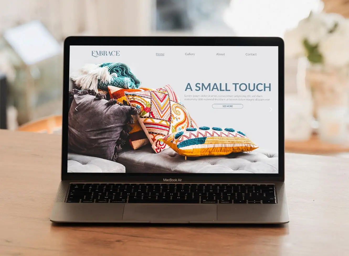 The Embrace website on a laptop, showing patterned cushions beside the headline A Small Touch