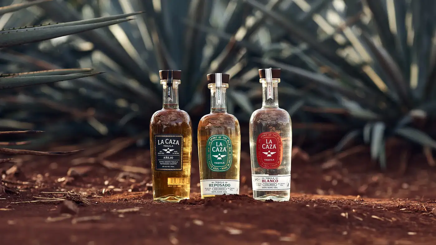 La Caza Blanco, Reposado and A\u00f1ejo standing in the red earth of a Jalisco agave field